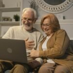 Happy senior couple sitting on a sofa having a joyful video call on a laptop in a cozy living room.